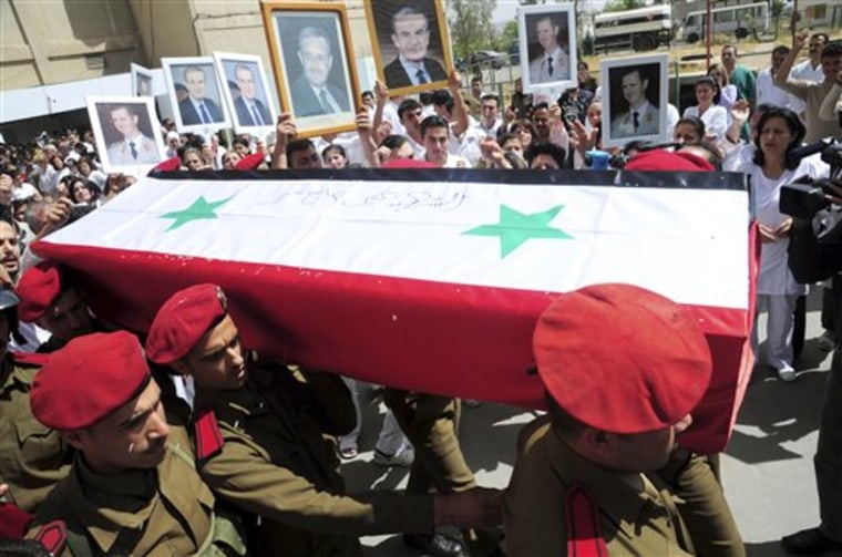 People carry pictures of Syrian President Bashar Assad and his father late President Hafez Assad as Syrian military police carry a coffin preparing to send the bodies of slain soldiers and security force members to their hometowns for burial in Damascus, Syria.